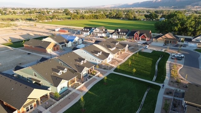 Drone view of a neighborhood showing colorful homes, surrounding green spaces, and the scenic landscape. The image captures the beauty of residential design integrated with the natural environment. 